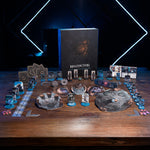 a collection of board games and game components arranged on a wooden table, with a focus on the game "Maldiction" and its accessories.