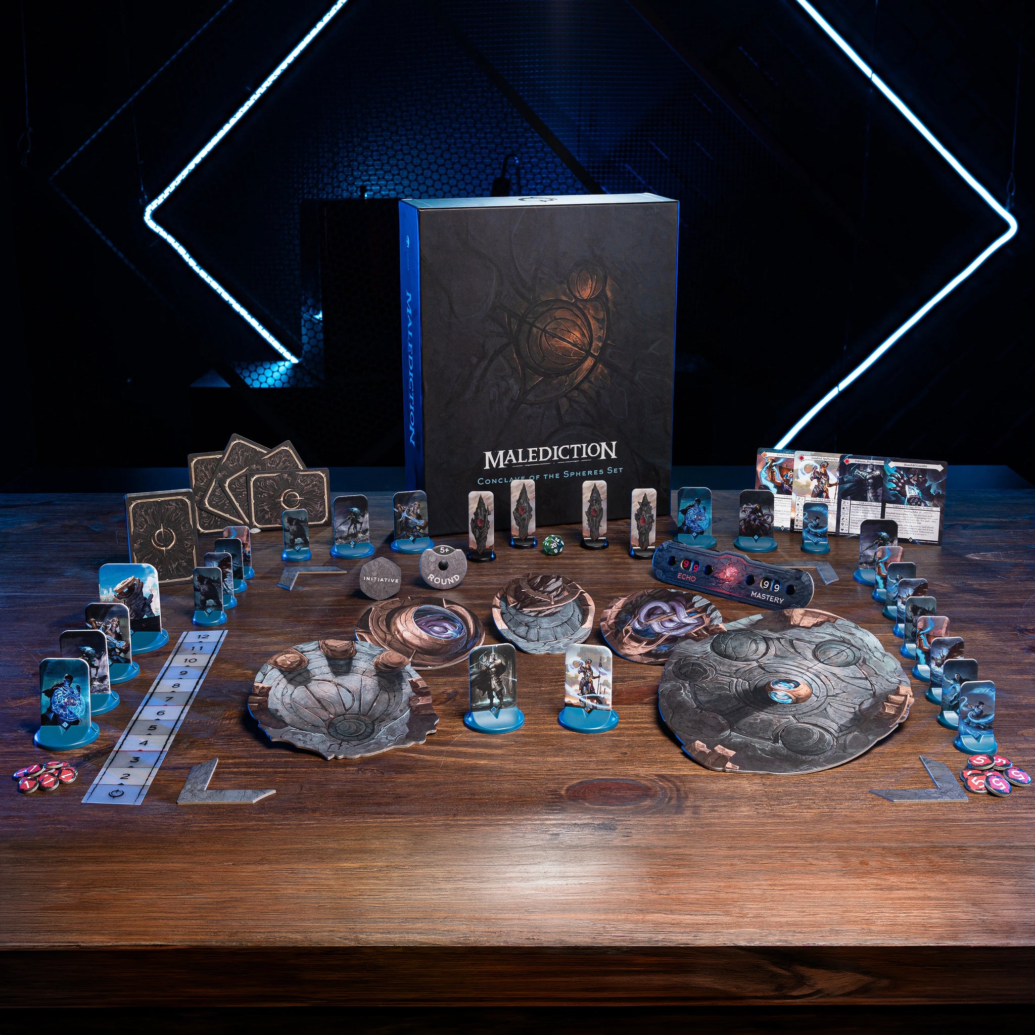 a collection of board games and game components arranged on a wooden table, with a focus on the game "Maldiction" and its accessories.